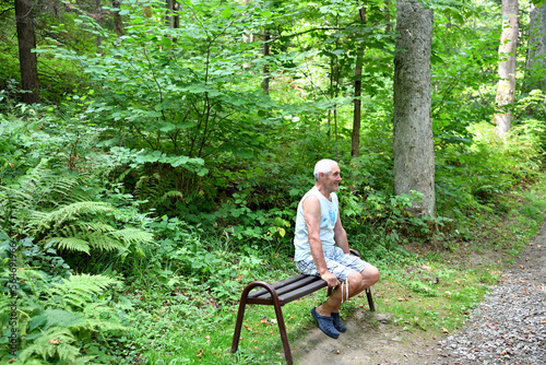 Tourist relaxing on a bench during a hike in the forest in hot summer