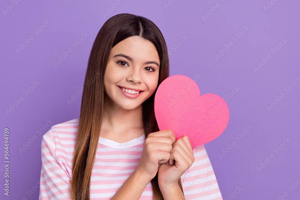 Photo of cheerful sweet girl beaming smile hands hold pink paper heart isolated on violet color background Photo of cheerful sweet girl beaming smile hands hold pink paper heart isolated on violet color background