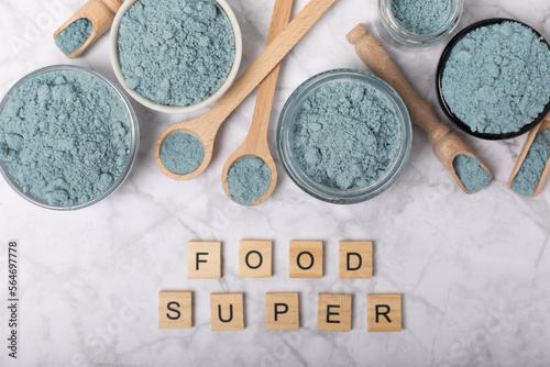 Blue spirulina powder in bowls and spoon on white marble background. Natural vegan superfood. food supplement. place for text. Copy space. photo