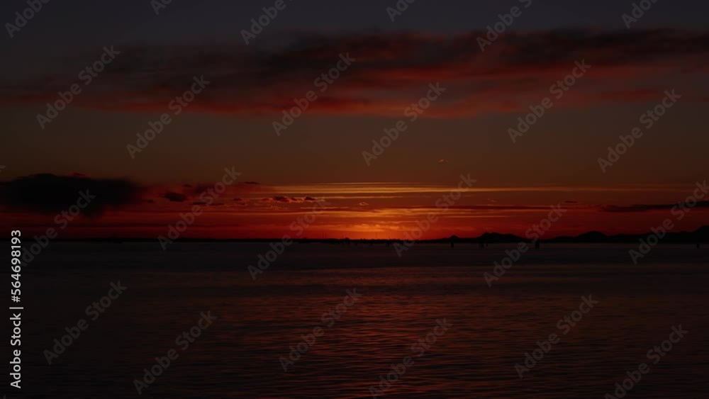 Boundless sea with rippling water under picturesque orange sky with massive cloud silhouettes after sunset in evening timelapse Boundless sea with rippling water under picturesque orange sky with massive cloud silhouettes after sunset in evening timelapse