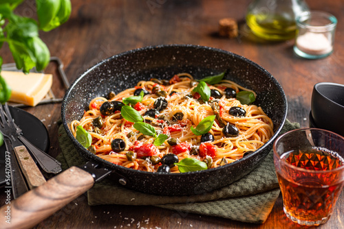 Spaghetti pasta with tomatoes sauce, black olives, capers, parmesan and fresh basil. Dark wooden table background