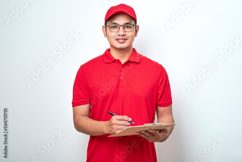 Young smiling asian delivery man in red uniform and cap holding clip board