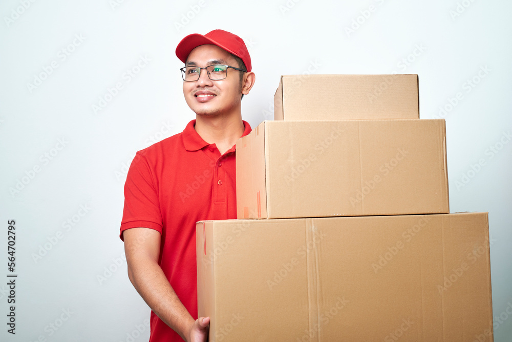 Dreamy smiling asian male courier in blue uniform, looking upper left corner excited and happy, carry boxes with orders, deliver parcels