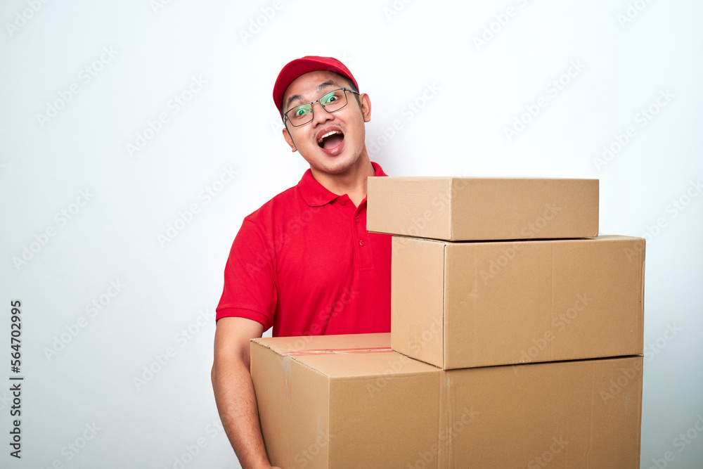 Smiling happy asian delivery man in red courier uniform, looking behind boxes with client orders, carry parcels to client home Smiling happy asian delivery man in red courier uniform, looking behind boxes with client orders, carry parcels to client home