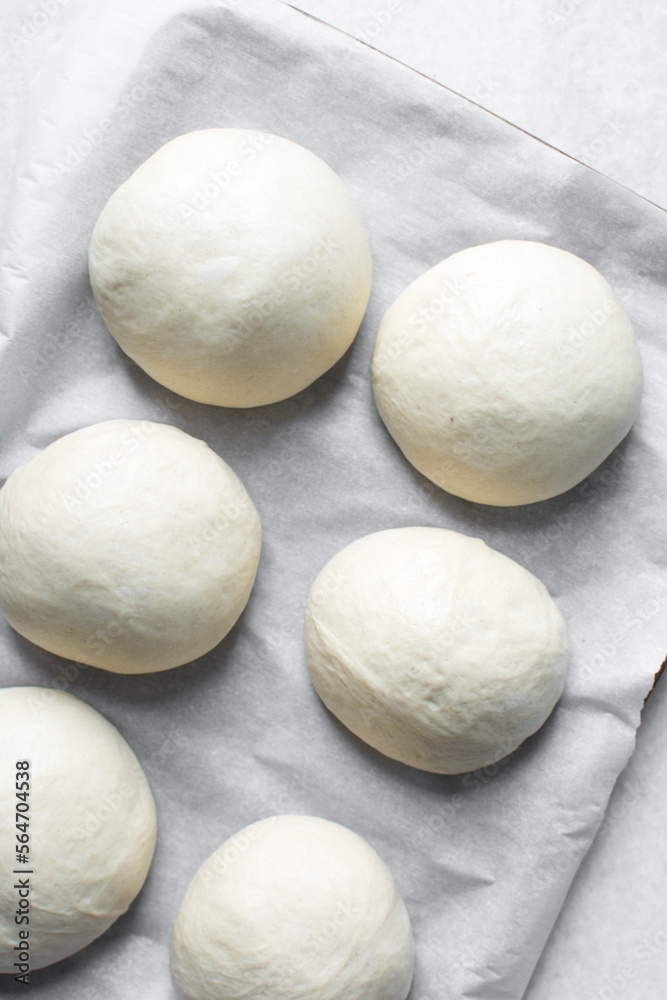 Bread bun dough that has doubled in size, dough that has risen, proofed dough on parchment lined baking sheet Bread bun dough that has doubled in size, dough that has risen, proofed dough on parchment lined baking sheet