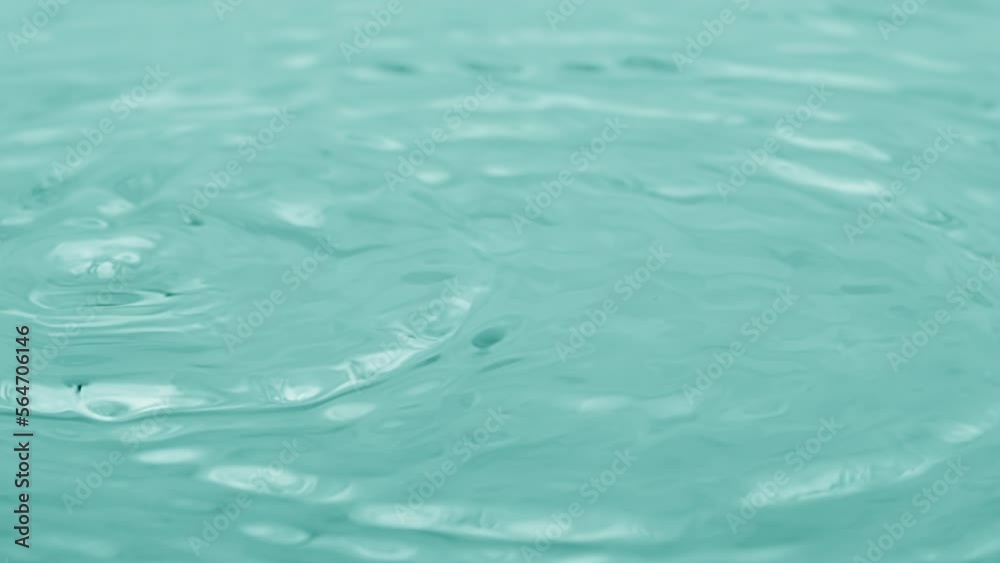 Macro crane shot of water drops fall down on water surface creating water rings on cyan background | Skin moisturizing concept