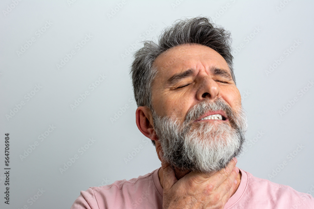 Fototapeta premium Mature man having sore throat and touching his neck, wearing a loose pink t-shirt against light grey background. Hard to swallow