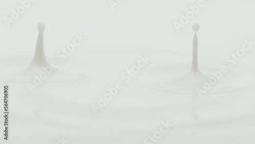 Macro crane shot of white opaque liquid is dripped splashing and creating ripples on white background | Skincare cosmetics with coconut milk commercial photo