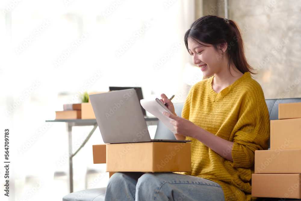 Happy Asian online business owner prepares packages and checks online orders of delivery items for customers using laptop computer to check details. online shopping concept. Happy Asian online business owner prepares packages and checks online orders of delivery items for customers using laptop computer to check details. online shopping concept.