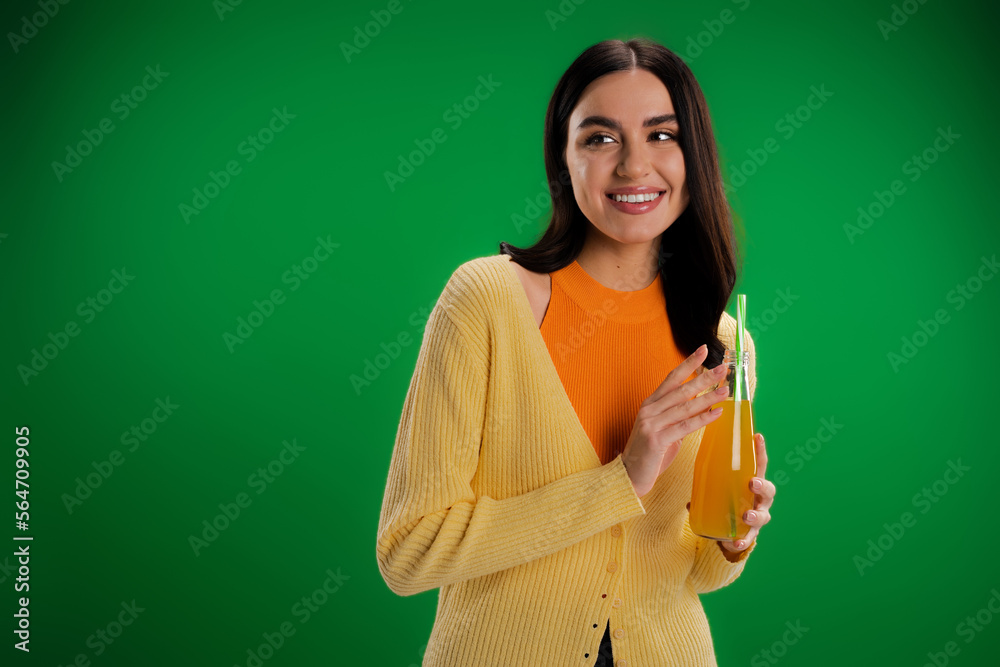 stylish woman with bottle of fresh juice smiling and looking away isolated on green. stylish woman with bottle of fresh juice smiling and looking away isolated on green.