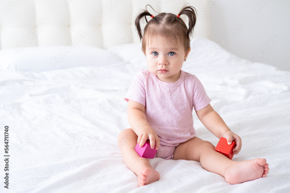 funny baby girl in pink bodysuit playing with children wooden cubes toys on bed funny baby girl in pink bodysuit playing with children wooden cubes toys on bed