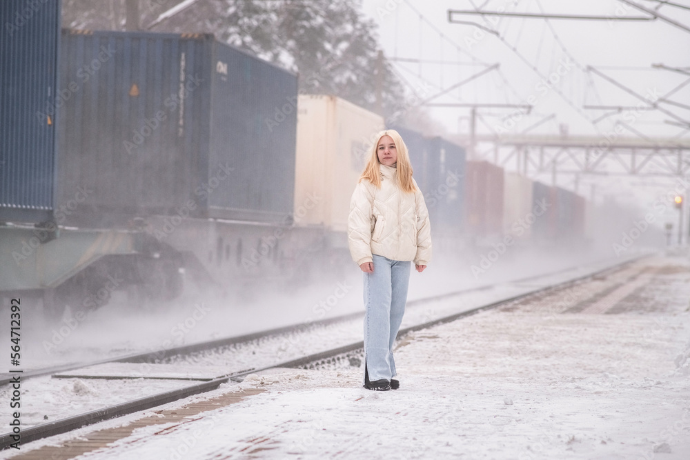 Portrait of a young beautiful fair-haired girl in the winter on the platform, a freight train passes by.