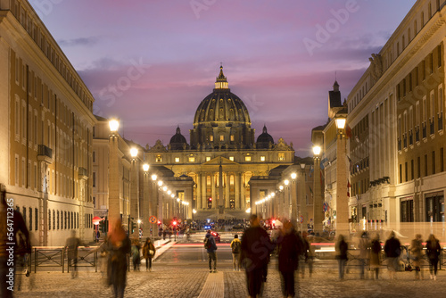 View of Illuminated Saint Peter`s Basilica and Street Via della Conciliazione at sunset with people on the street. Rome, Italy Europe