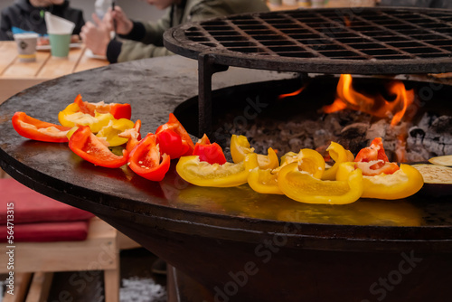 Process of grilling healthy sliced red, yellow sweet bell pepper on brazier at summer outdoor food market - close up. Professional cooking, barbecue, gastronomy and street food concept