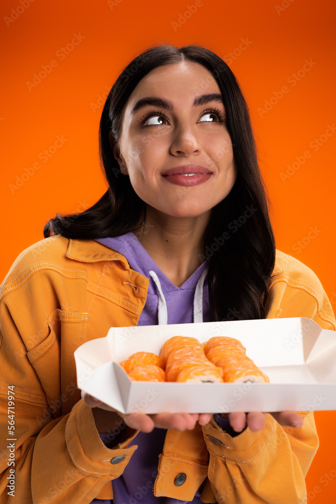 Portrait of dreamy young woman holding takeaway sushi isolated on orange. Portrait of dreamy young woman holding takeaway sushi isolated on orange.
