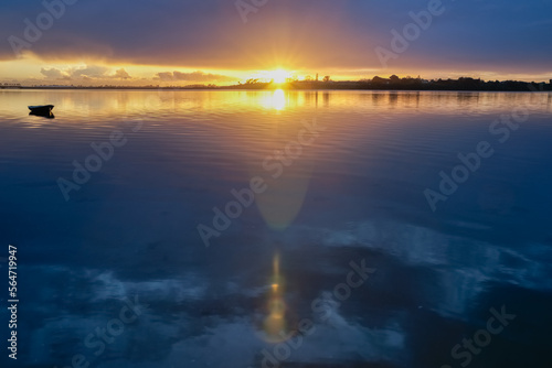 Intense deep sunrise with sunburst and lens flare effect over habour with small dinghy at anchor