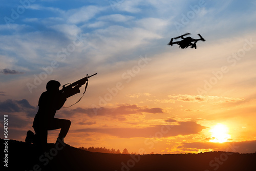 Soldier trying to shoot down reconnaissance drone against the backdrop of a sunset. Soldier shoots a quadcopter. Modern methods of warfare. Technology concept.