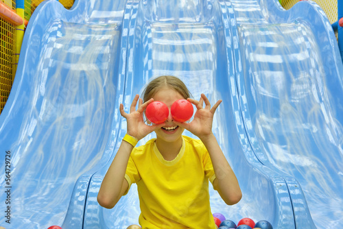 A funny girl is having fun playing with colorful balls in the game center and riding down a slide