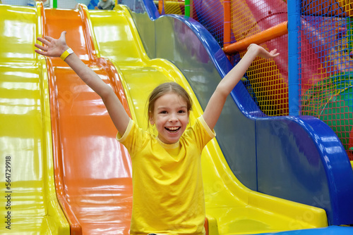 A happy cheerful girl child rides down a slide in a game center, in an amusement park for her birthday