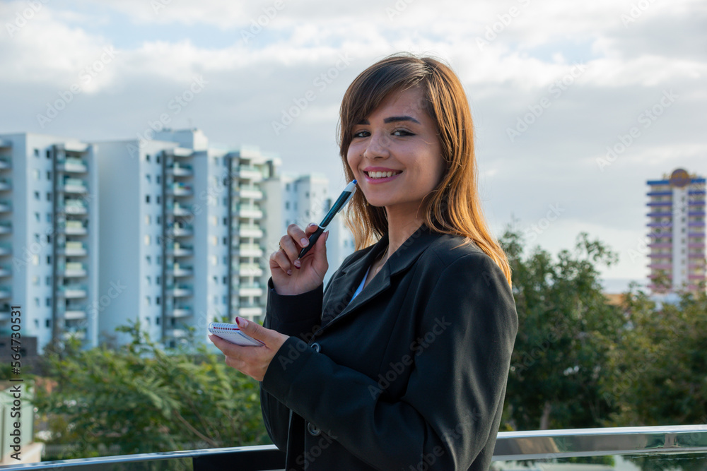 Smiling businesswoman takes notes in her notebook on the terrace of her office. Smiling businesswoman takes notes in her notebook on the terrace of her office.