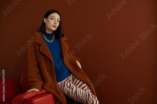 Fashionable confident woman wearing trendy blue turtleneck, brown faux fur coat, chunky chain, trousers with zebra print. Studio fashion portrait. Copy, empty space for text photo