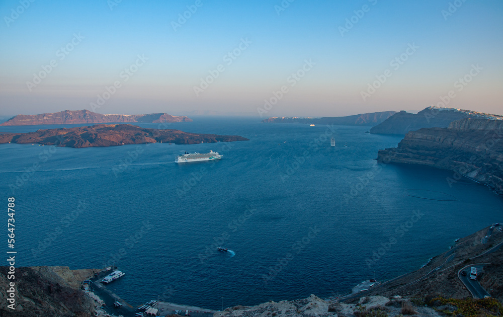 A beautiful landscape of Santorini Islands at sunrise with cruise ships and boats going by in the bay and a harbor and Road below