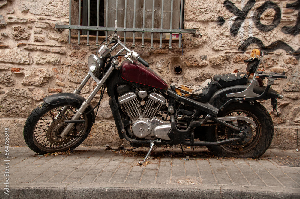 An old beat-up motorcycle against a stone wall with a window that has bars on it