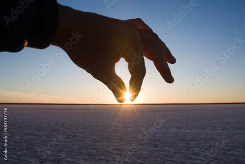 A hand pinches the setting sun over the salt flats on Laguna San Ignacio, Baja California, Mexico. photo
