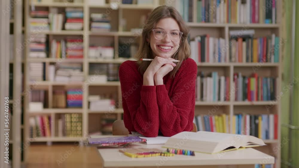 A young beautiful female student smiles into the camera while studying in the library—medium shot. A young beautiful female student smiles into the camera while studying in the library—medium shot.