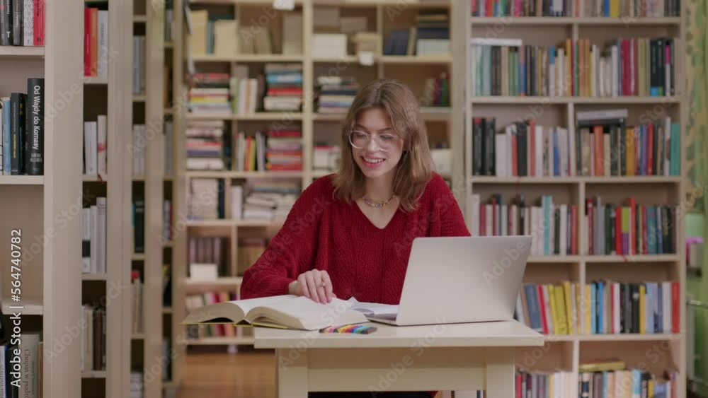 Caucasian student with glasses doing research in library using laptop Caucasian student with glasses doing research in library using laptop