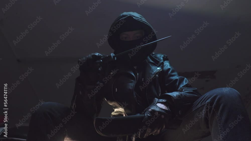 Criminal with bandit mask and black leather gloves inspects knife
