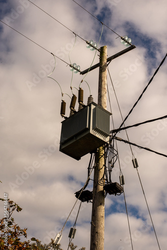 AC high voltage power transformer. Transfer of electrical power to end users through wooden pole distribution transformer that switches high voltage to low voltage against the backdrop of blue sky.