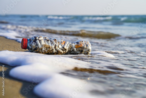 A bottle of cigarette butt stub on the clean beach sand near mediterranean sea and ocean, to pay attention to environmental pollution, global warming and warning