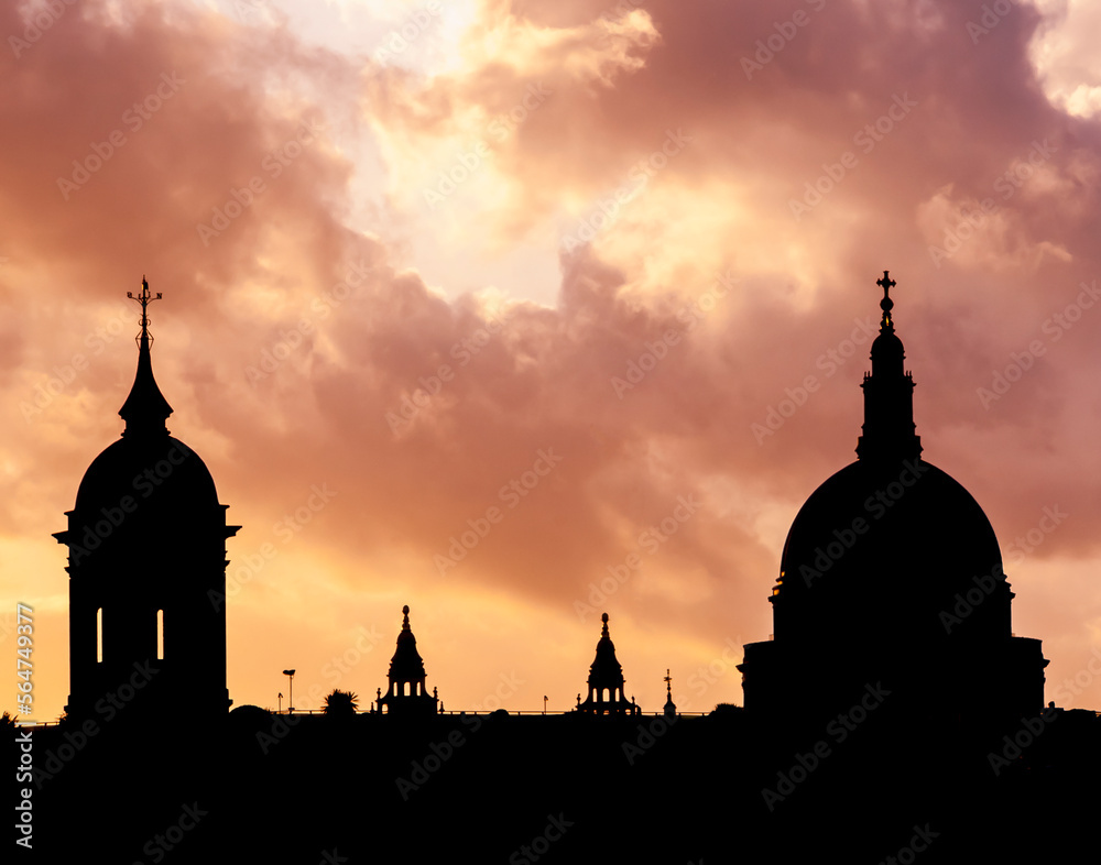 Silhouettes of dome tops of building against a dramatic orange evening sky in London England.