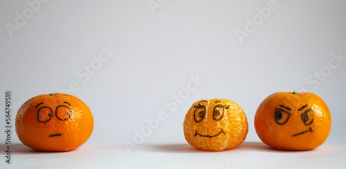 Three tangerines with drawn emotions.  One looks suspiciously and askance at a couple where a friendly girl is next to a disgruntled guy.  photo