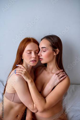 two half-naked lesbian lgbtq models on bed, hugging, touching each other, at home in the morning. Sensual young caucasian women in underwear in modern apartment showing true emotion.