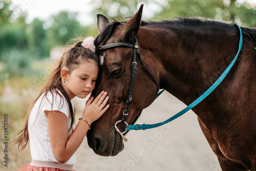 Cute little girl stroking a horse's head on a farm in the countryside in summer. Love for horses. © sergo321