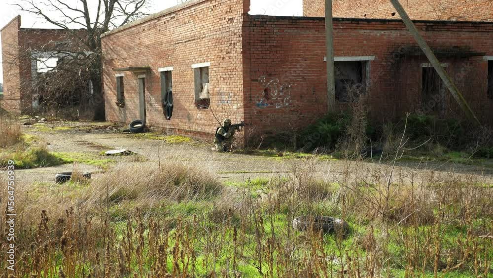 A soldier in camouflage uniform and military uniforms stands on one knee and takes aim with a rifle against the background of a destroyed building. Airsoft. A soldier in camouflage uniform and military uniforms stands on one knee and takes aim with a rifle against the background of a destroyed building. Airsoft.
