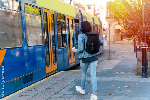 a young smiling woman in a denim jacket drinking coffee and waiting for a tram at the stop Lifestyle photo