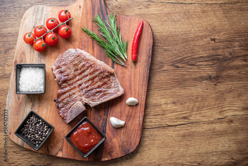 Fototapeta Naklejka Na Ścianę i Meble -  grilled T-bone steak on a cutting board with herbs on a wooden background with copy space for your text.