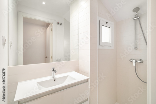 Petite but bright bathroom with shower  large mirror and sink  and a small window that gives some natural light. The clean white tiles and minimalistic design give the space a fresh and modern feel