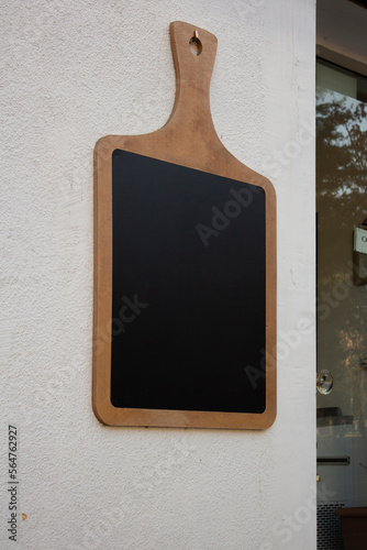 Vertical photo. Wooden cutting board on white wall of restaurant with glass door. Black chalk board. Mock up space. Place for text. Offer. Street cafe menu. Catering concept. Copyspace. Public. Pub