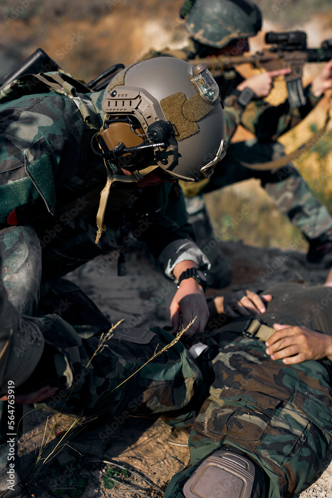 brave fearless soldier man help comrade on fight area, injured guy lying on ground with a sore wounded leg, soldier raising it trying to save the life. military forces, war, army concept