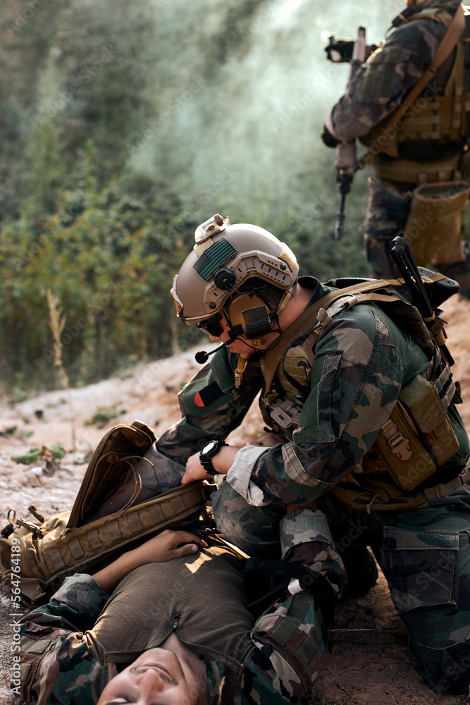 Responsive european caucasian soldier help injured comrade lying on ground, in mountains, another soldier calls for halp in the background. Fully equipped military forces in operations.