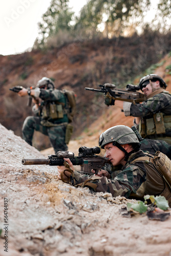 team of military soldiers, shooters wearing combat uniform, body armor and helmet, aiming service rifles, covering each other while moving in trench. Infantrymen on battlefield, fight against enemy