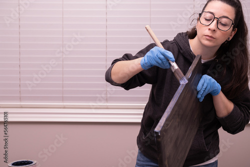 recognizable woman applying varnish with a brush, wearing gloves and glasses