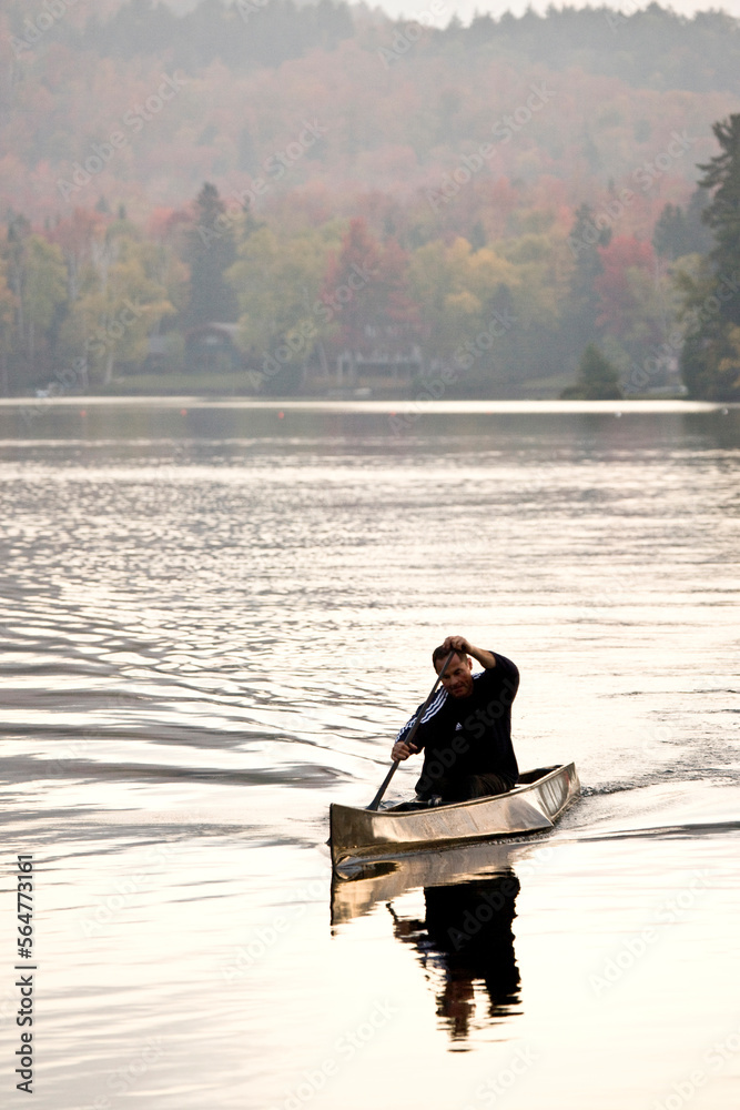Young man paddles race canoe on Mirror Lake, Adirondacks, upstate New York, USA. Young man paddles race canoe on Mirror Lake, Adirondacks, upstate New York, USA.