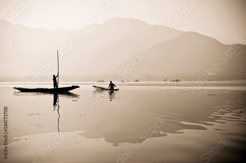 A toned black and white photograph of a traditional Kashmiri shikara, or gondola, reflected in a mirror-calm, Dal Lake, Srinagar, Kashmir, India. photo