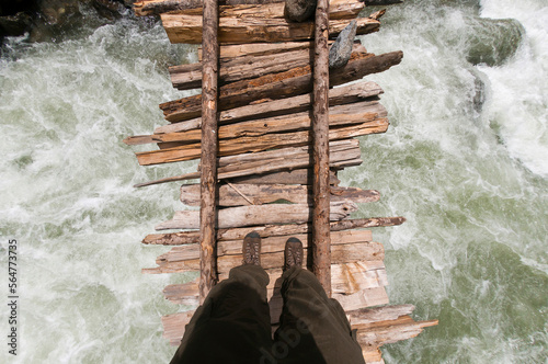 A point of view shot looking down of trekker crossing the swollen Kanka River on a rickety wodden bridge, Naranag, Gangabal Lake region, Kashmir Himalayas, India
