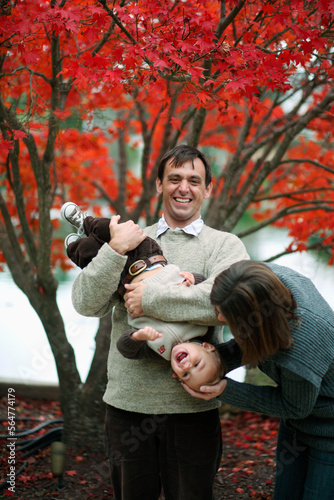 A mother, chid and father play under colorful leaves on trees.